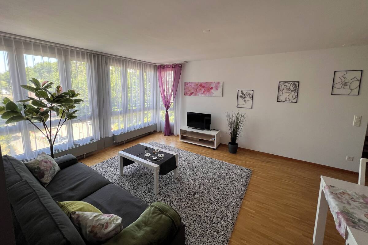 Ein modernes Wohnzimmer mit Sofa, Couchtisch, Fernseher und Kunstwerken an der Wand.