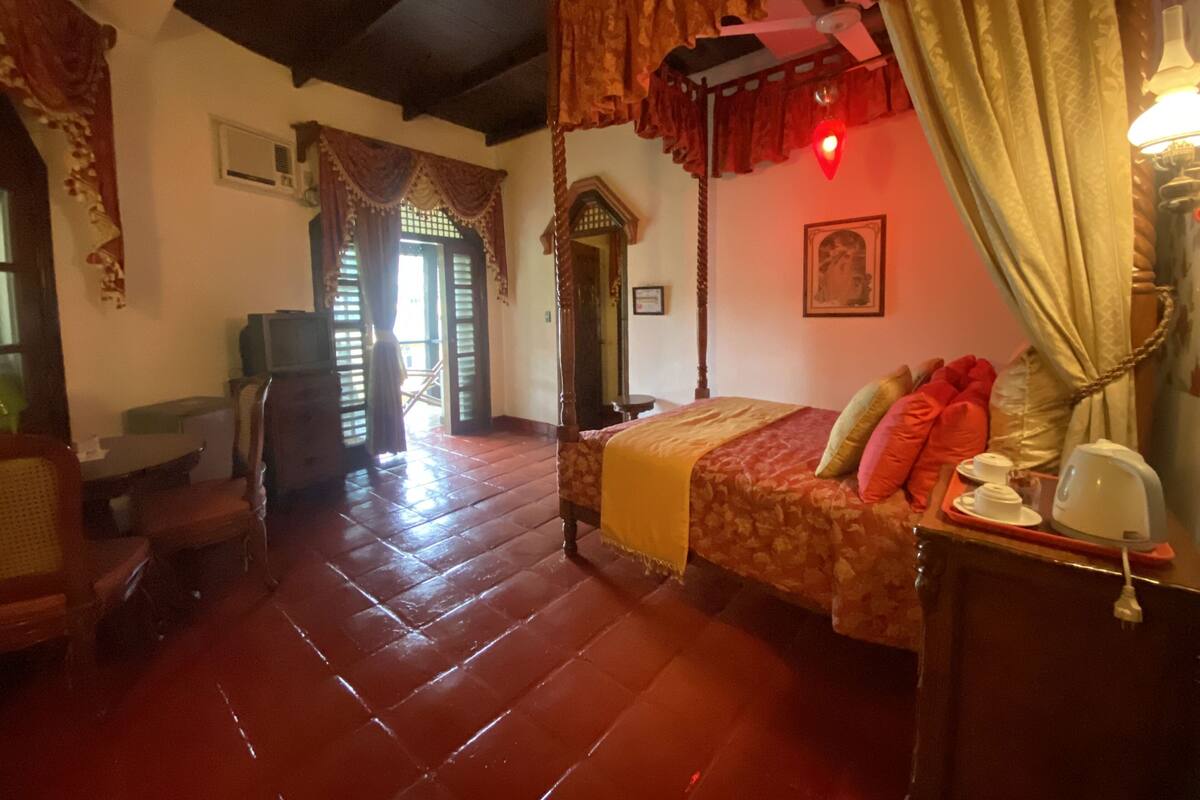 Ein traditionell eingerichtetes Zimmer mit Himmelbett, Holzboden und Blick durch eine Tür nach draußen.