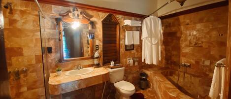 Un baño con piso de mármol, lavamanos, inodoro, ducha y cabina de ducha con paredes de vidrio.
