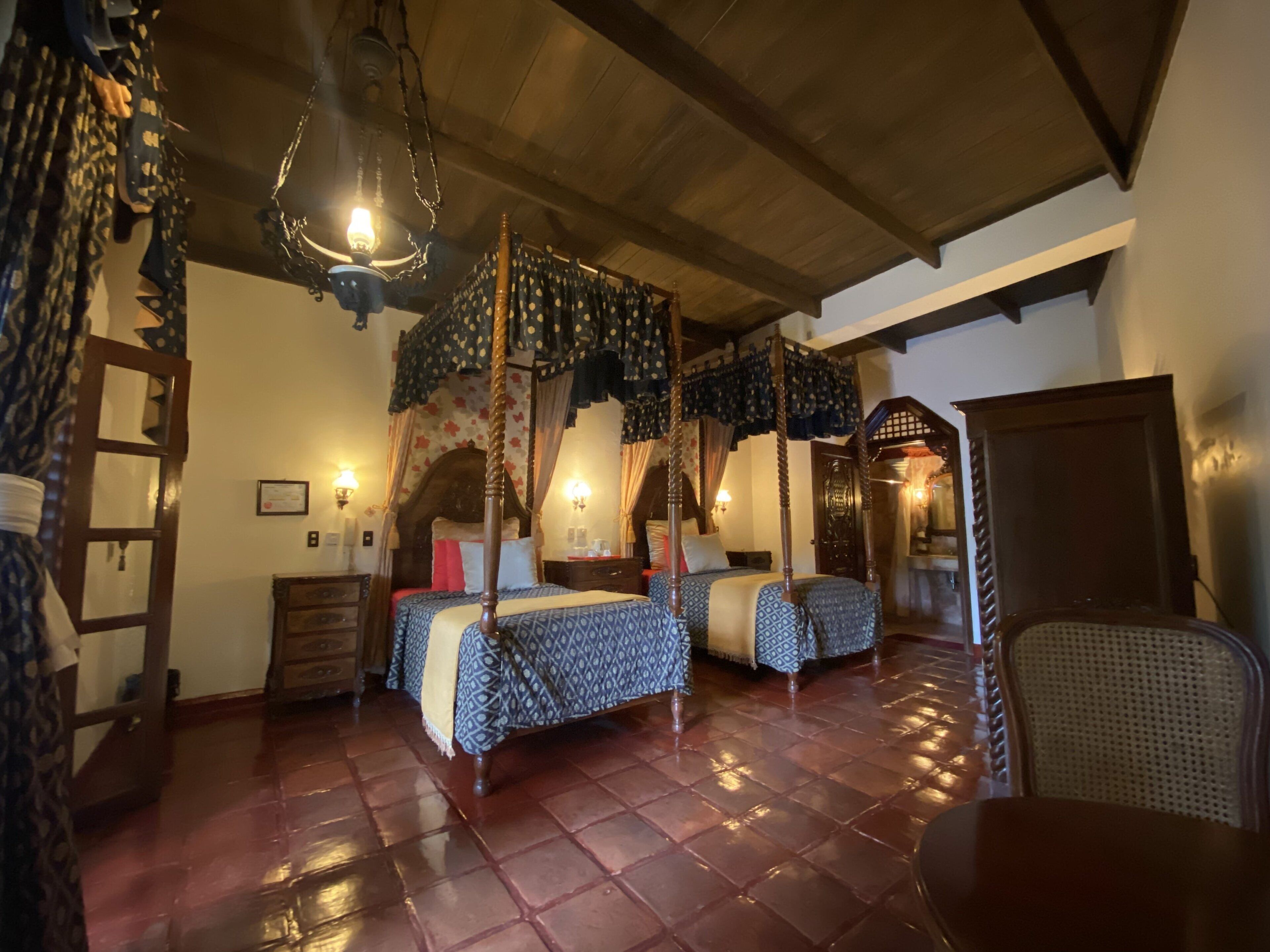 A traditional bedroom with a four-poster bed, two smaller beds, a wooden ceiling, and a tiled floor.