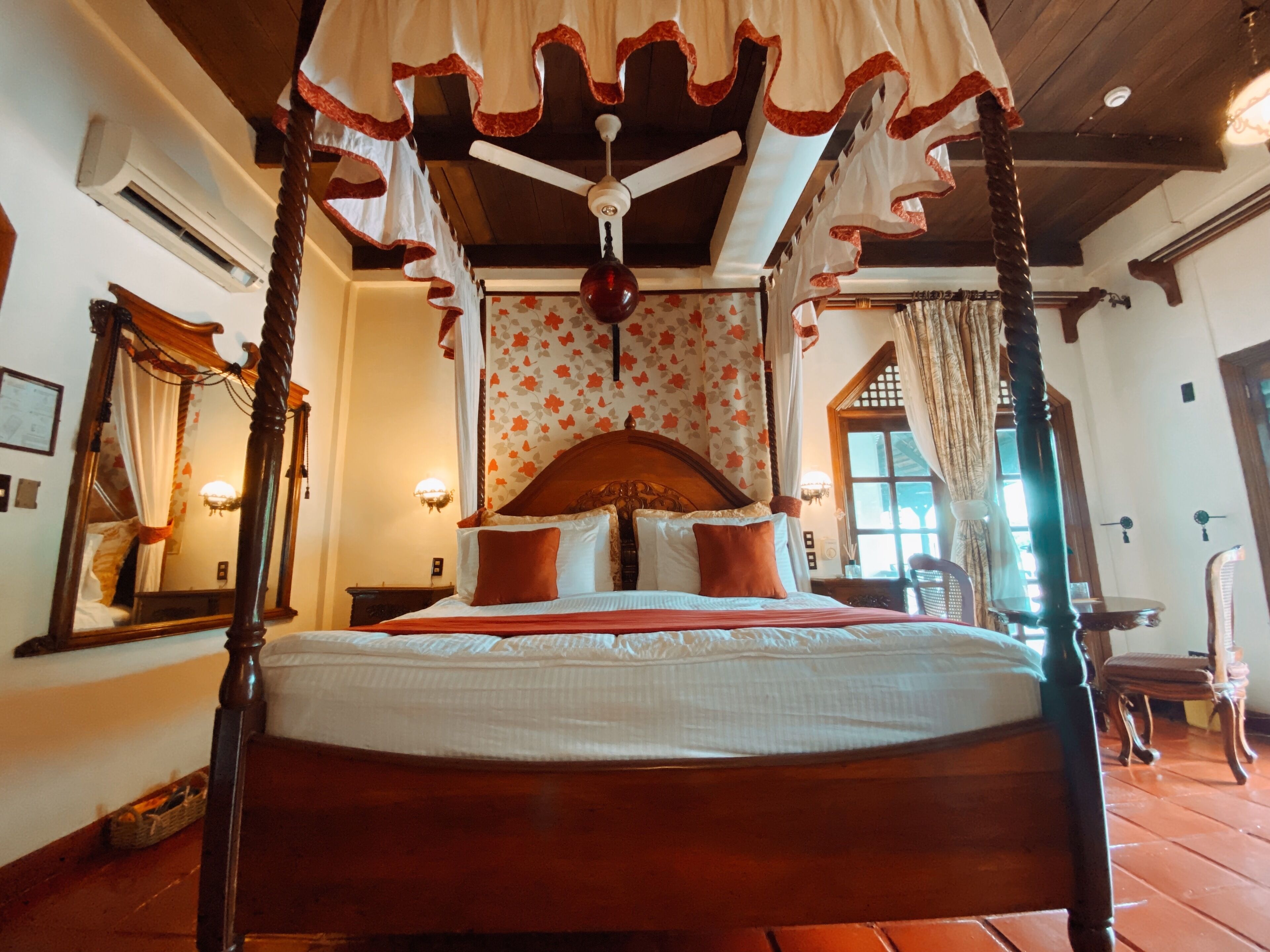 A four-poster bed with a canopy, a wooden ceiling, and a floral wallpaper pattern.