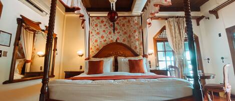 A four-poster bed with a canopy, a wooden ceiling, and a floral wallpaper pattern.