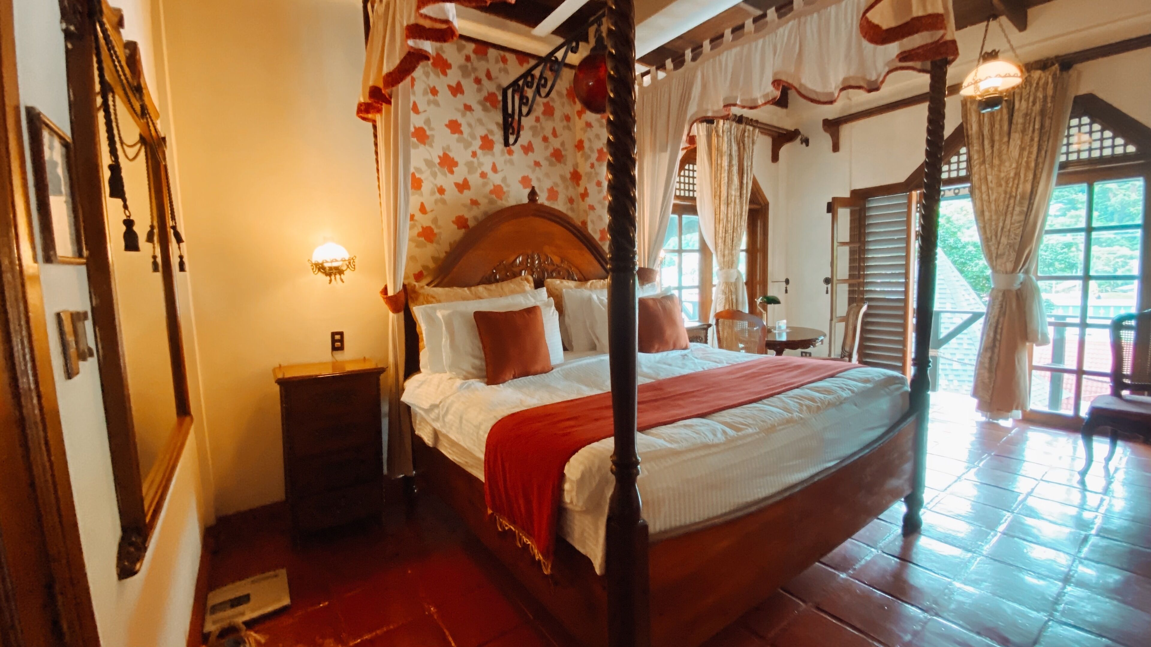 A four-poster canopy bed with a wooden headboard, a nightstand, and a window with curtains.