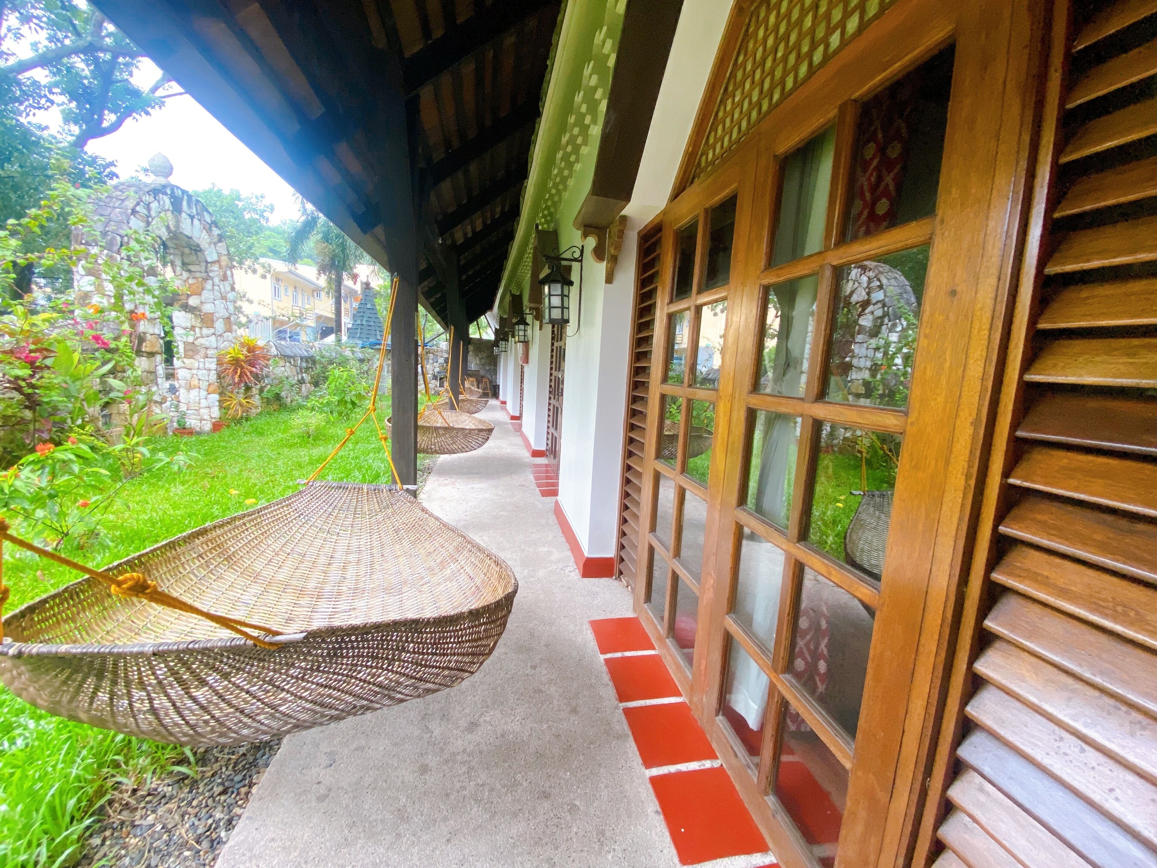 A covered walkway with wicker chairs, a stone wall, and a view of greenery.
