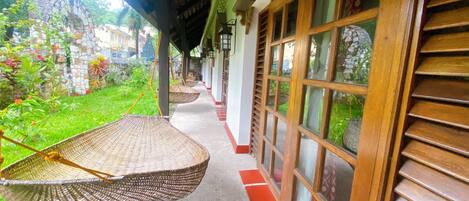 A covered walkway with wicker chairs, a stone wall, and a view of greenery.
