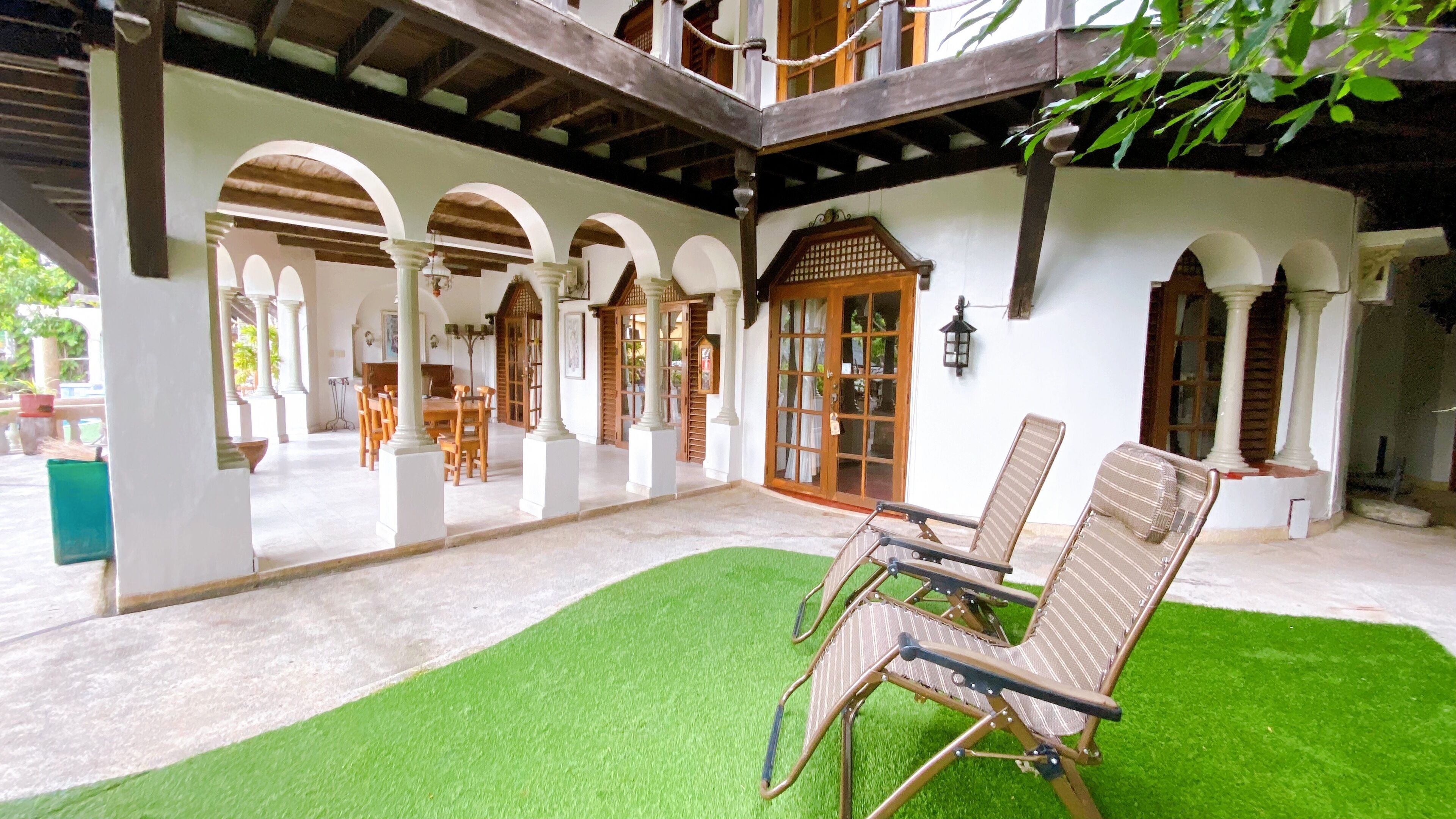 A covered outdoor area with a dining table and chairs, surrounded by white pillars and wooden doors.