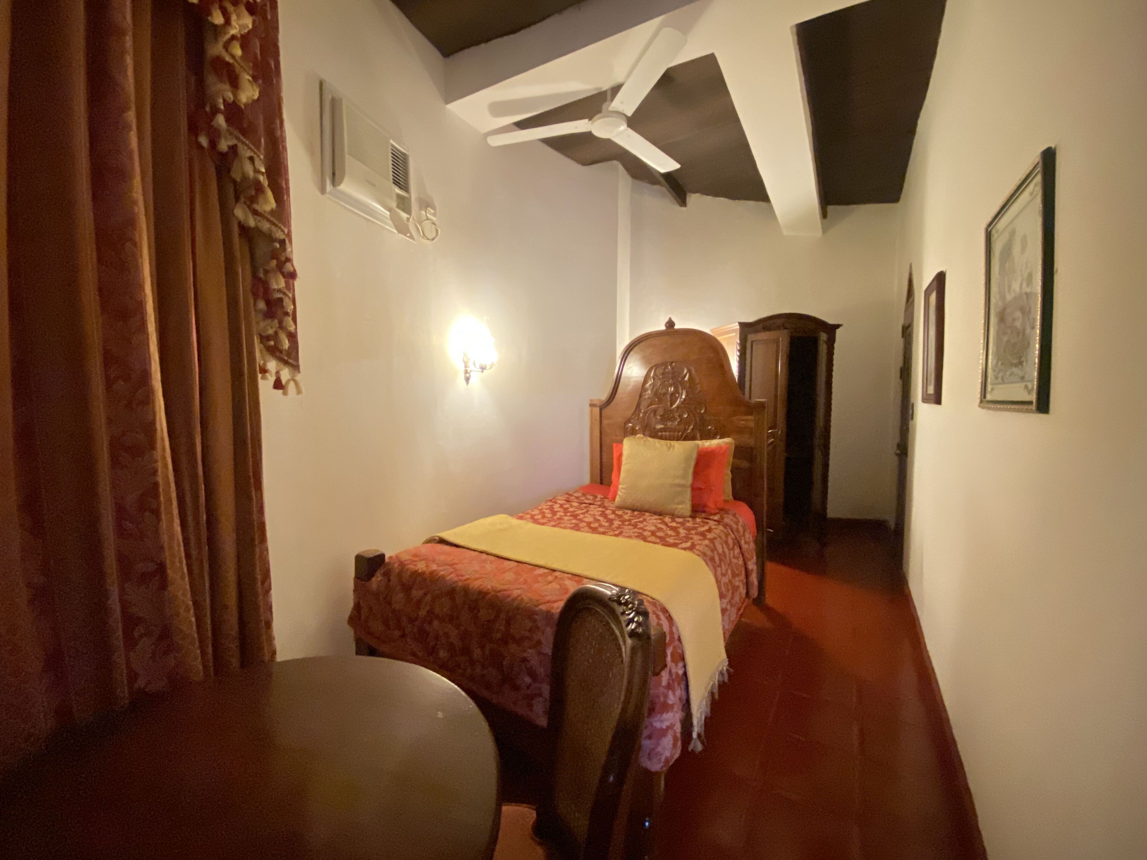 A bedroom with a wooden bed, a chair, a desk, a ceiling fan, and a wall-mounted light fixture.