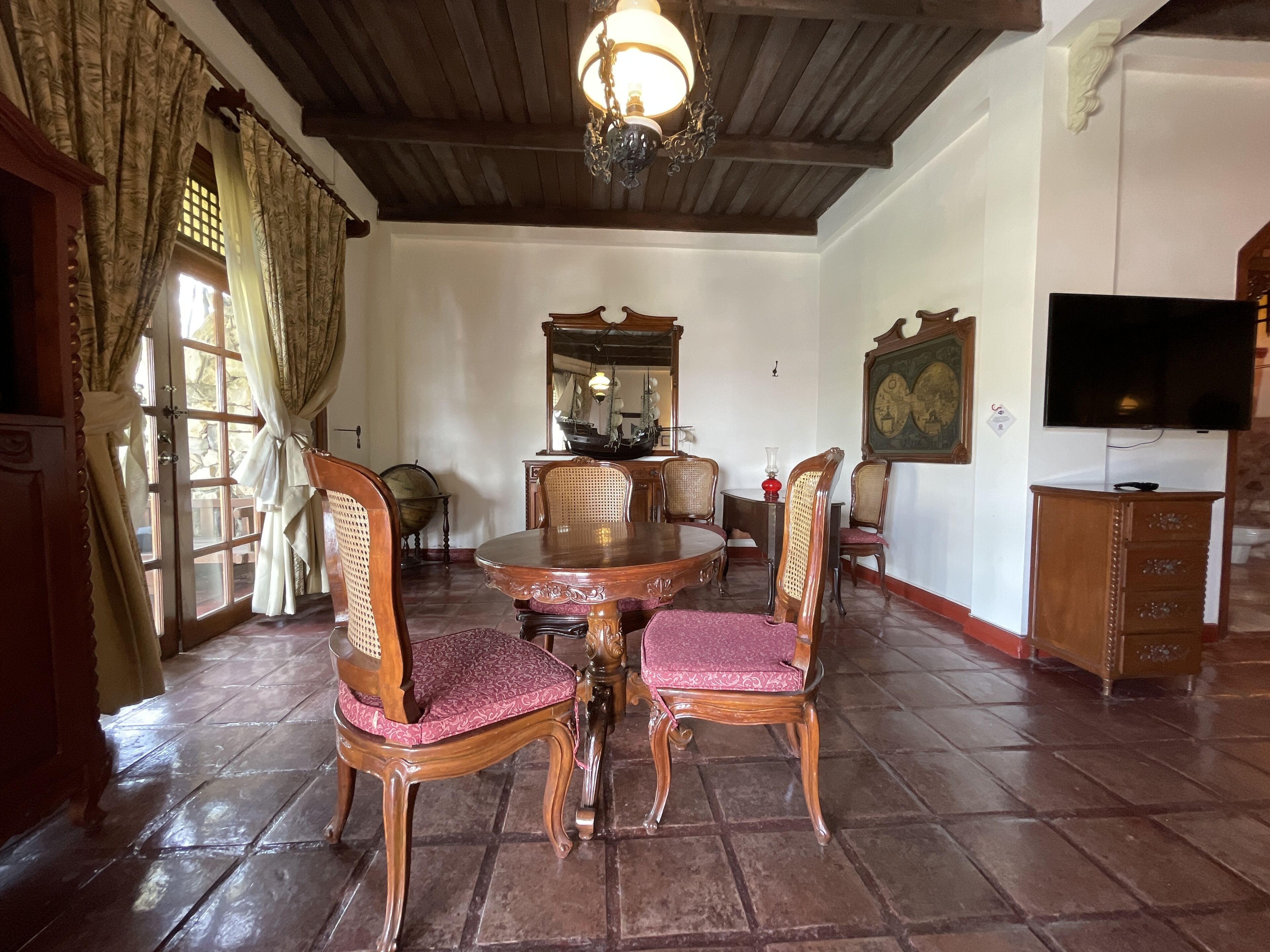 Un comedor con una mesa y sillas de madera, una araña, un globo terráqueo y un televisor.