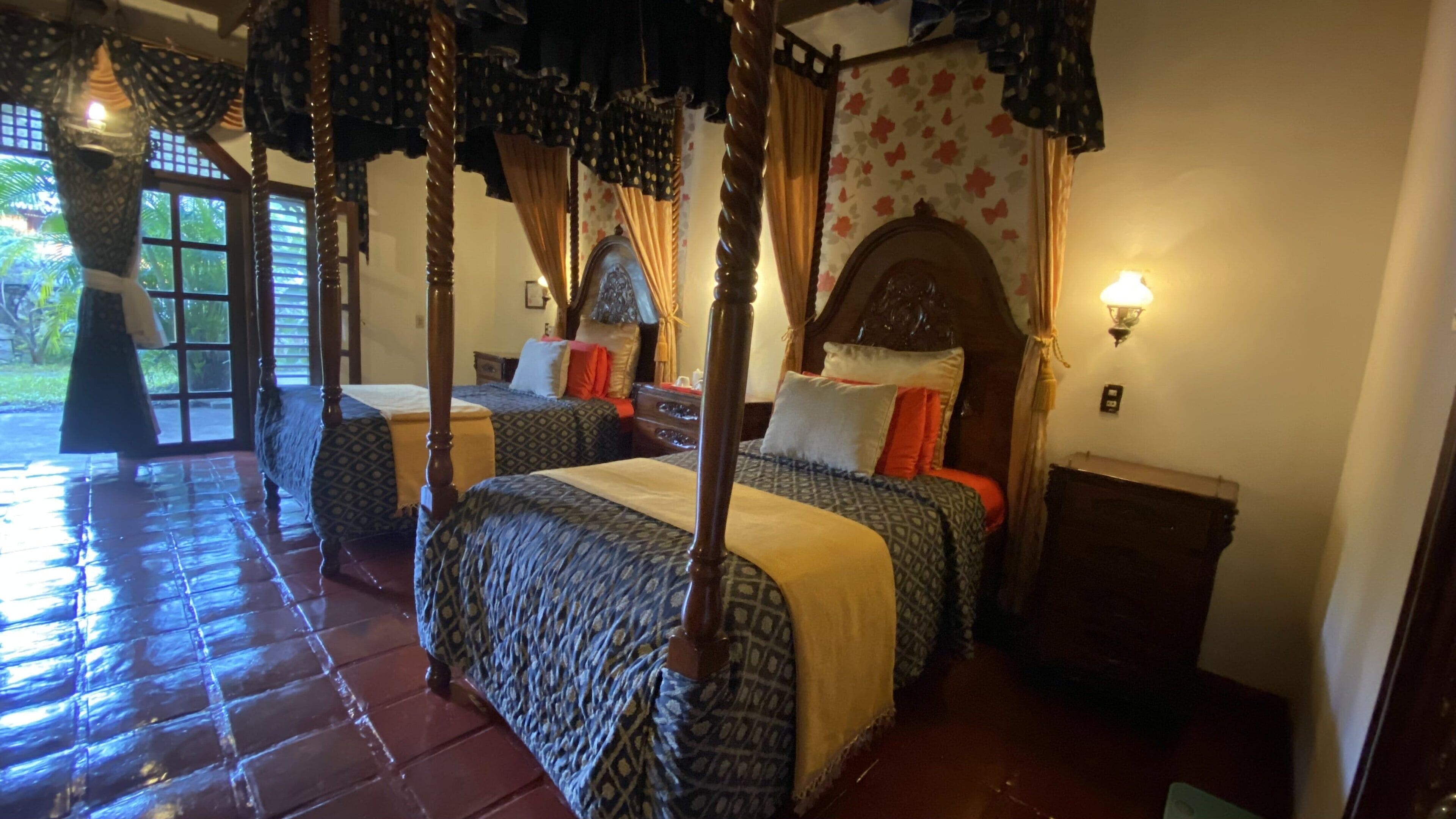 A traditional four-poster bed with a canopy, two bedside tables, and a floral-patterned wall.