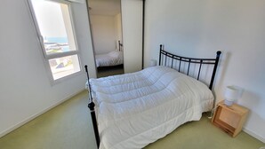 A bedroom with a bed, a window, a door leading to another room, and a small bedside table with a lamp. - T2 apartment with terrace, 500m from the beach, Les Sables-d'Olonne (Les Sables-d'Olonne)