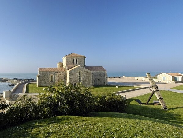 A stone church with a bell tower, a grassy area, and a view of the sea.