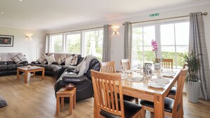 Ein geräumiges Wohnzimmer mit einer schwarzen Ledersofa, einem Holzespeisetisch für vier Personen und einem großen Fenster mit Blick auf Grünfläche.