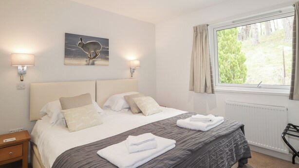 Ein Schlafzimmer mit einem großen Bett, zwei Nachttischlampen, einem Fenster mit Vorhängen, einem Heizkörper und einem Bild von einem Kaninchen an der Wand.
