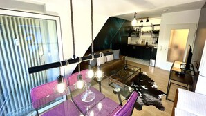 A modern living space with a glass dining table, purple chairs, a leather sofa, a cowhide rug, and a kitchen in the background. - Boutique Apartment Petite Belle (Freiburg im Breisgau)