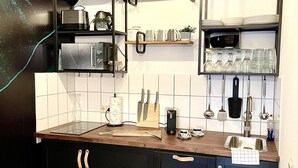 A modern kitchen with black cabinets, a wooden countertop, and a hanging shelf above the sink. - Boutique Apartment Petite Belle (Freiburg im Breisgau)