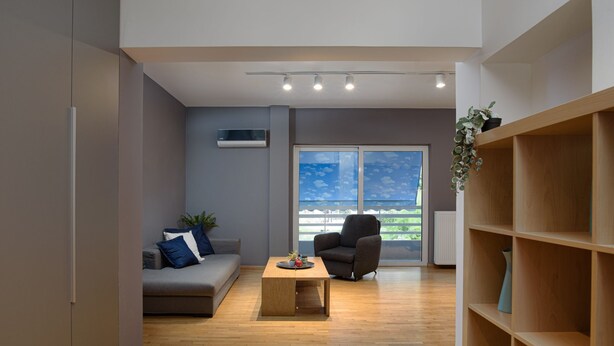 Una sala moderna con un sofá gris, un sillón negro y una mesa de centro de madera. Hay una ventana grande con vistas a follaje exterior.