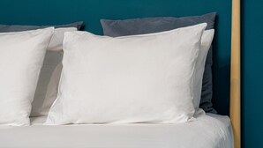 Una cama con almohadas blancas y grises, un cabecero de madera y una pared color turquesa.