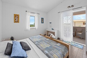 A bedroom with a bed, a bedside table, a window with curtains, and a view of the outside.
