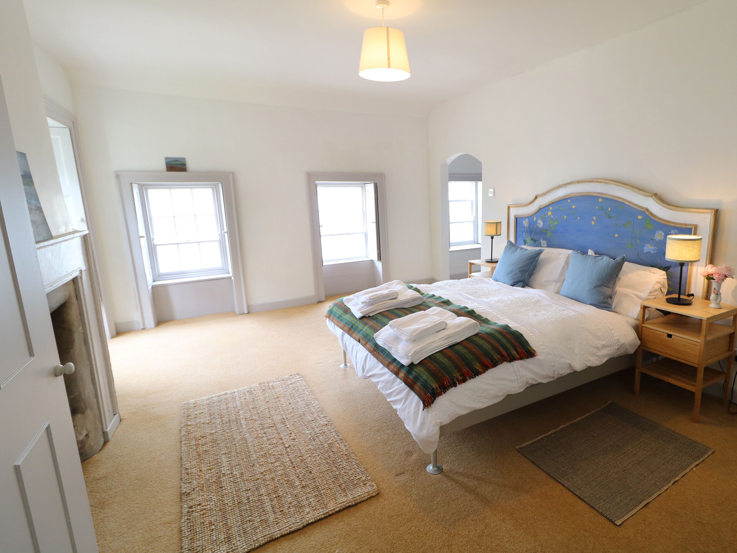 Quarto com cama, mesas de cabeceira, abajur e janela.