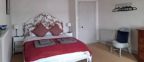 Une chambre à coucher comprenant un lit, une table de chevet, une chaise, une commode et un radiateur.