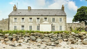 A stone building with multiple windows and a central entrance, surrounded by a rocky landscape. - The Ferry House (Ramelton)