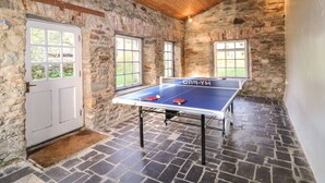 A ping pong table in a stone-walled room with wooden beams on the ceiling and a door with a window. - The Ferry House (Ramelton)