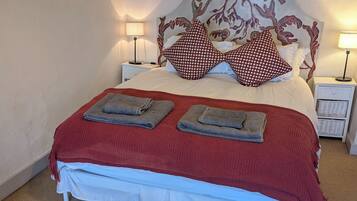 Una cama bien hecha con una colcha roja y blanca, dos toallas dobladas y un cabecero floral.