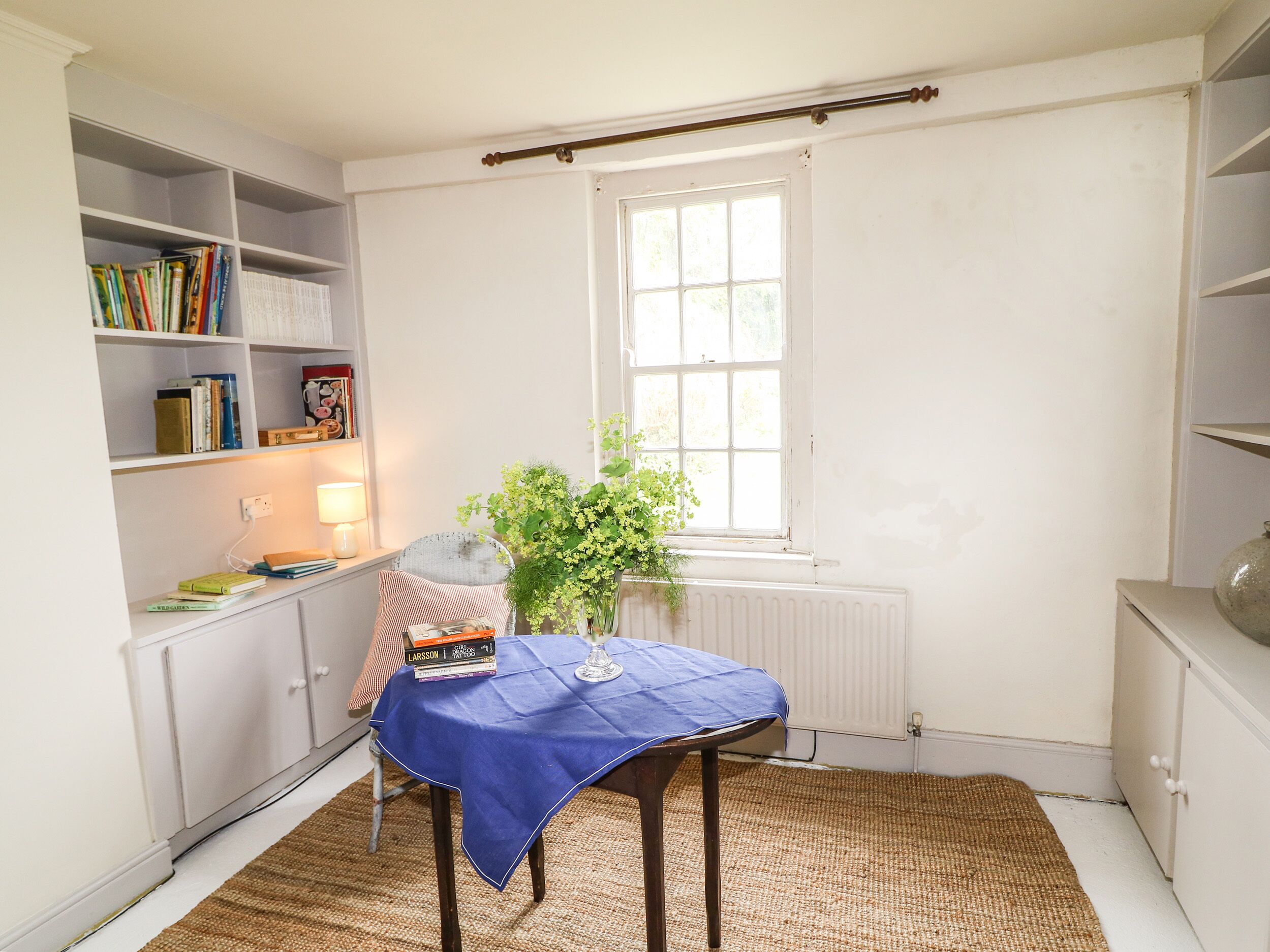 A room with a table, chair, bookshelf, radiator, window, and a plant.