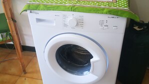 En tvättmaskin med frontmatning, och ovanpå ligger ett grönt, mönstrat bordsduk.