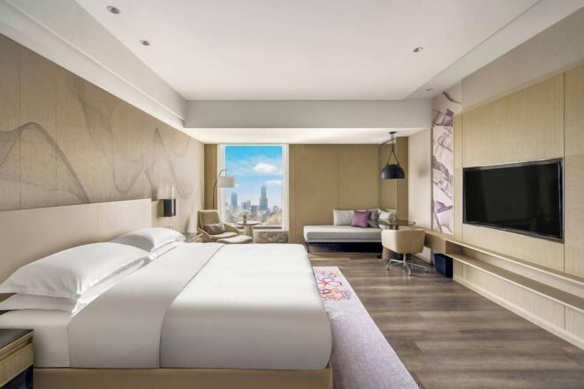 Una habitación de hotel moderna con una cama grande, televisión, vista a la ciudad y zona de estar.