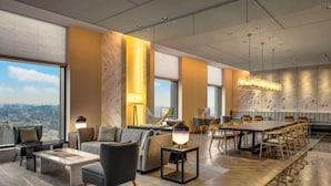 Un moderno vestíbulo de hotel con una amplia mesa de comedor, asientos cómodos y grandes ventanales con vista a la ciudad.