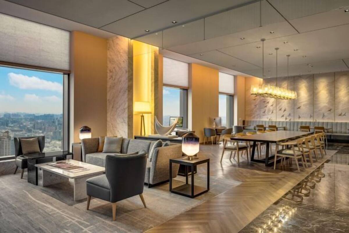 Un moderno vestíbulo de hotel con una amplia mesa de comedor, asientos cómodos y grandes ventanales con vista a la ciudad.