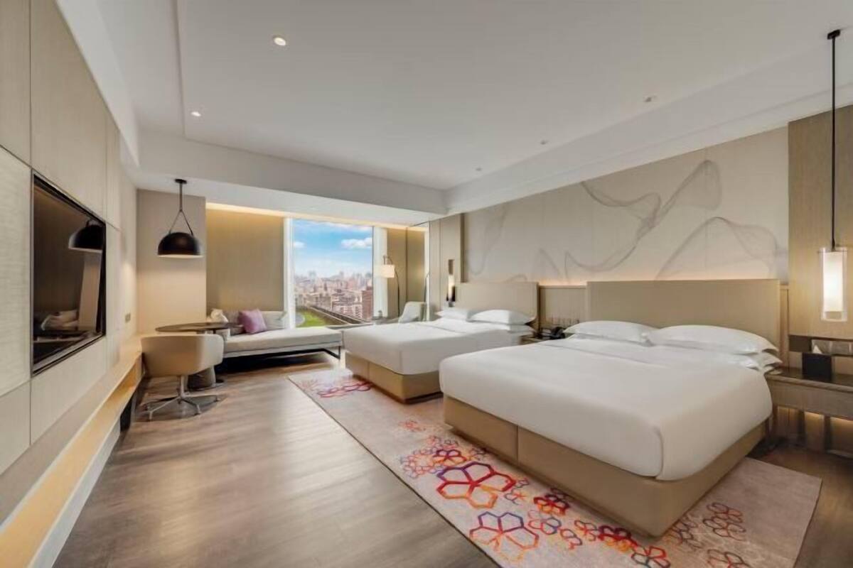 Habitación de hotel moderna con una cama grande, un sofá y un escritorio. Se ve la ciudad a través de la ventana.