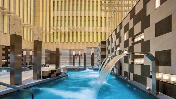 Una piscina interior con cascada, rodeada de arquitectura moderna con patrones de cuadros y líneas verticales.