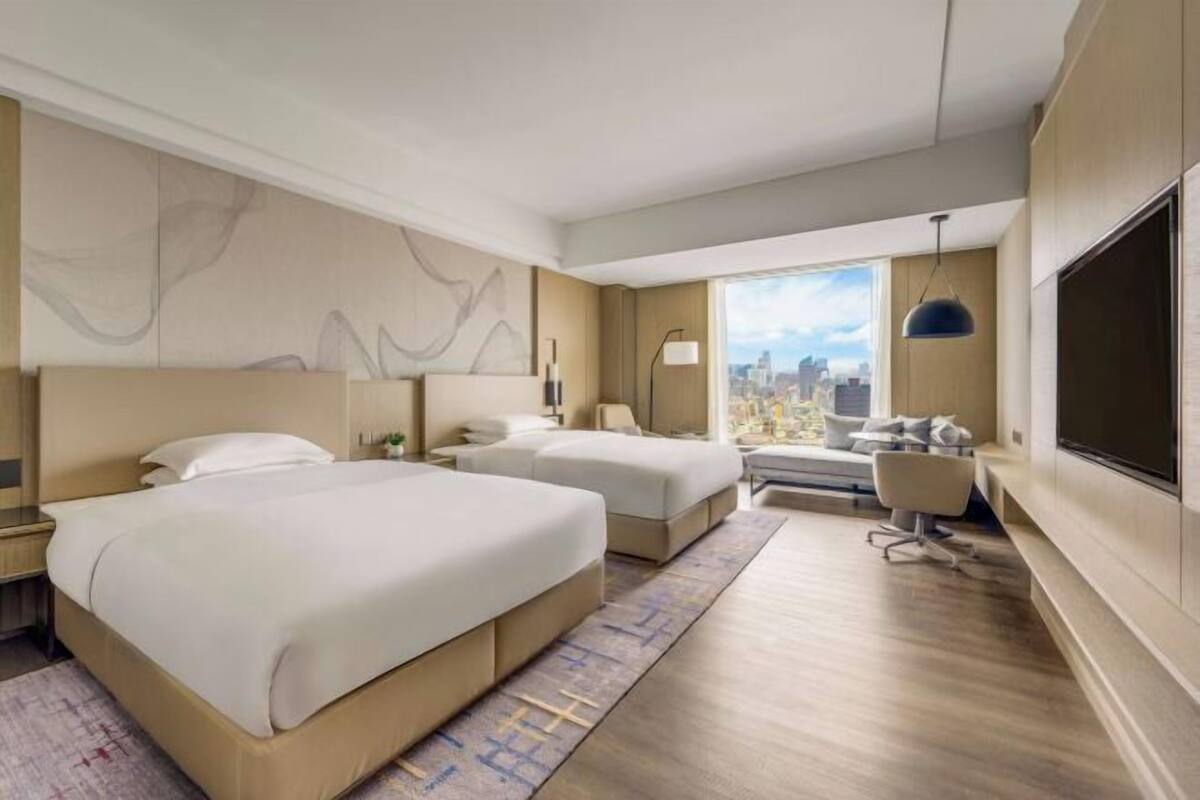 Habitación de hotel con una cama grande, un escritorio, una silla, un televisor y una ventana con vistas a la ciudad.
