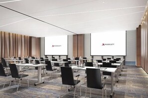 Ein Konferenzraum mit mehreren Tischen und Stühlen, einer großen Leinwand und dem Marriott-Logo.