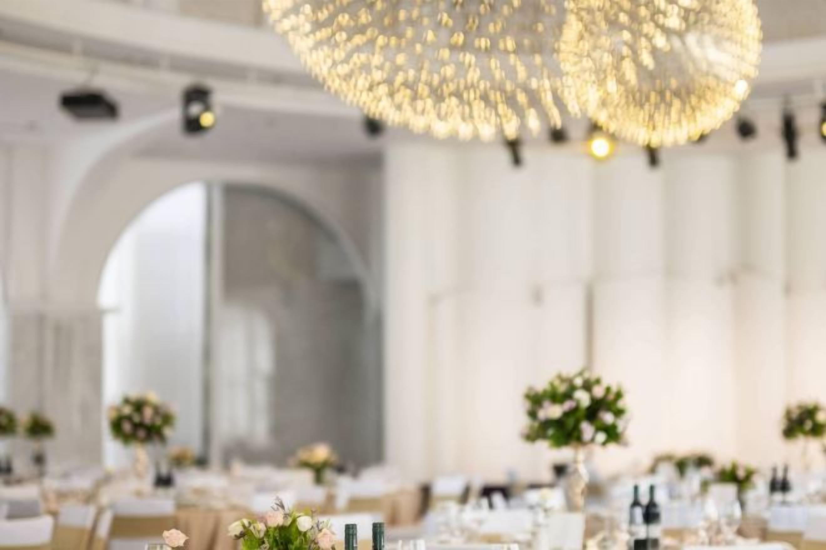 A banquet hall with tables set for a formal event, featuring a large chandelier and arched ceiling.