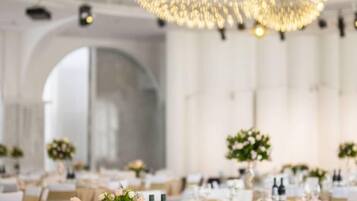 A banquet hall with tables set for a formal event, featuring a large chandelier and arched ceiling.
