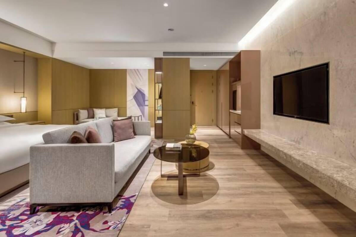 Una habitación de hotel moderna con cama, sofá, televisor y una mesa de centro redonda.