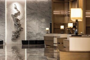 Eine moderne Hotelhalle mit einer Marmor-Rezeption, einer skulpturalen Wandgestaltung und stimmungsvoller Beleuchtung.