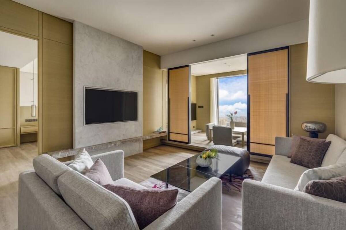 Una sala de estar moderna con una televisión de pantalla plana montada en la pared, una mesa de centro de vidrio y un sofá con cojines.