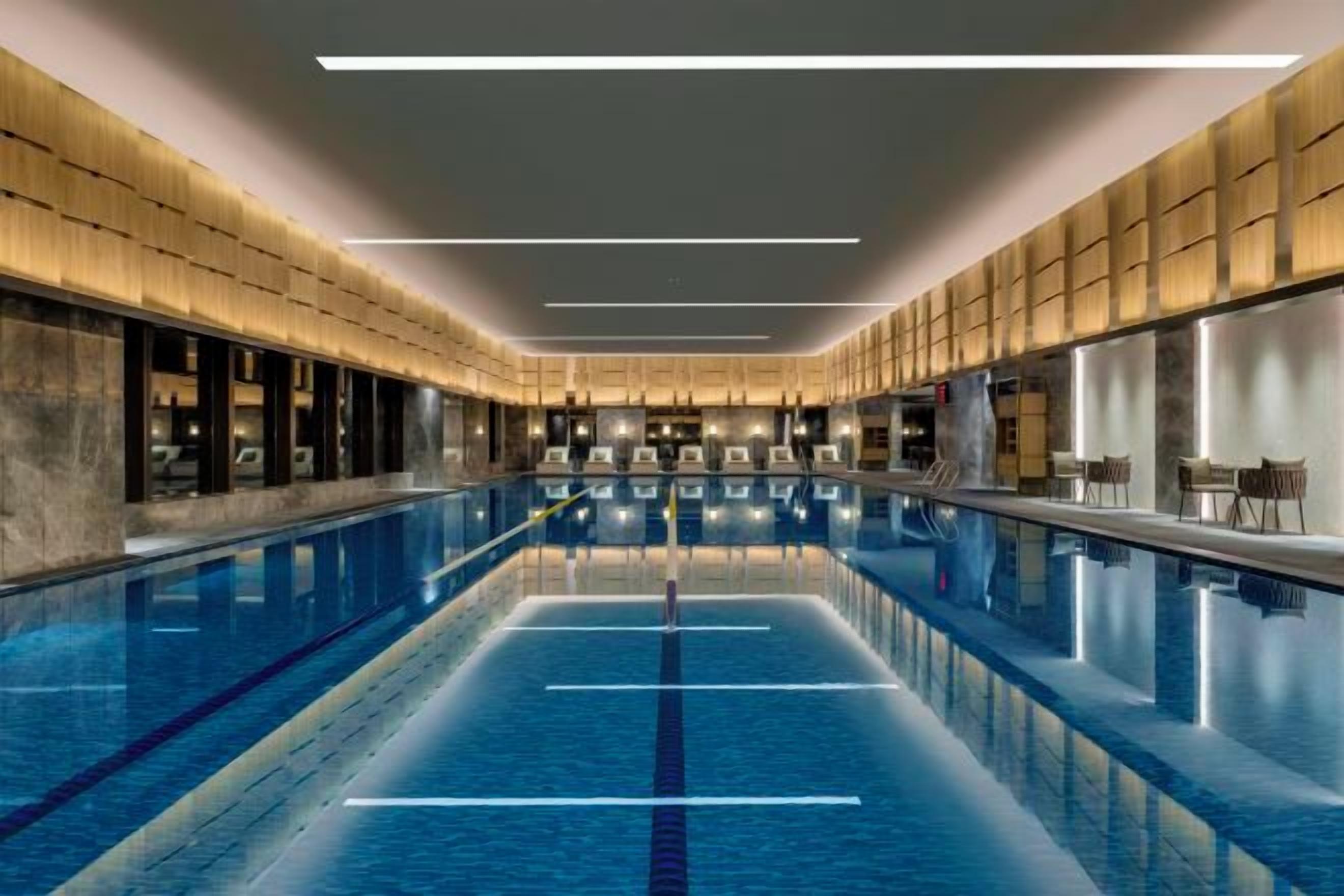 A long indoor swimming pool with clear lanes, surrounded by seating areas and a modern architectural design.
