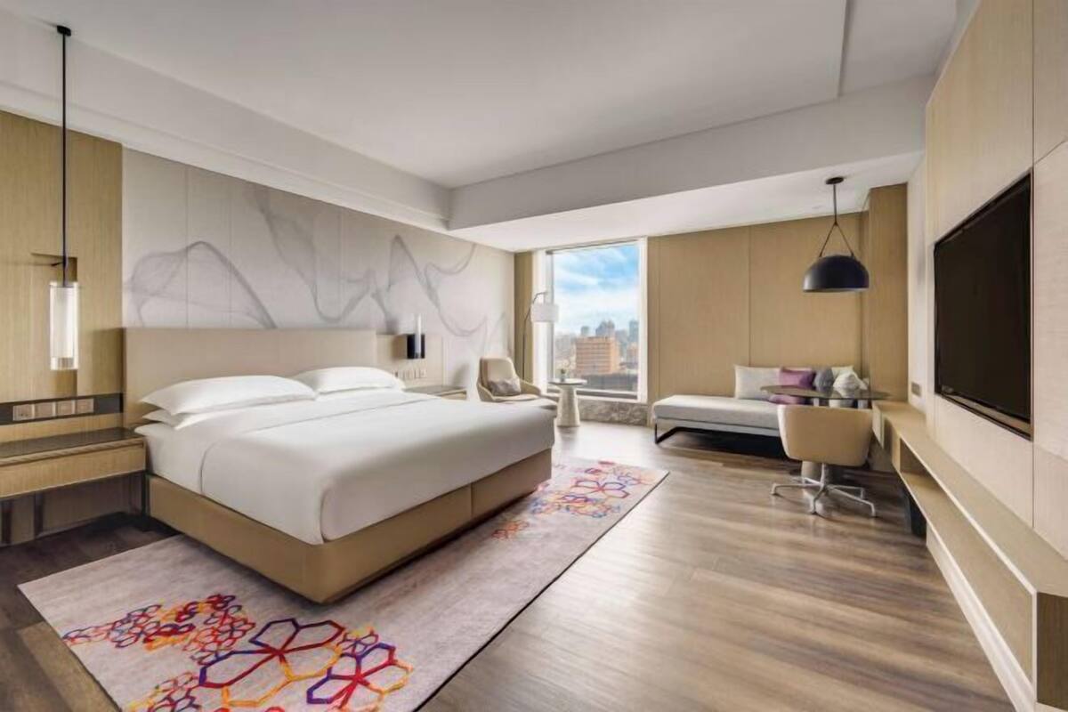 Una habitación de hotel moderna con una cama grande, televisión, escritorio y vistas a la ciudad.