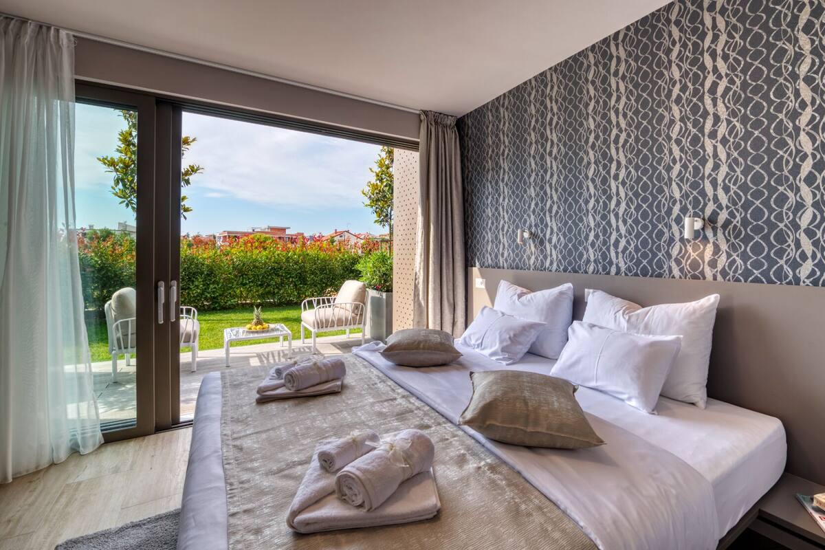A hotel room with a large bed, a view of a garden, and a patterned wall.