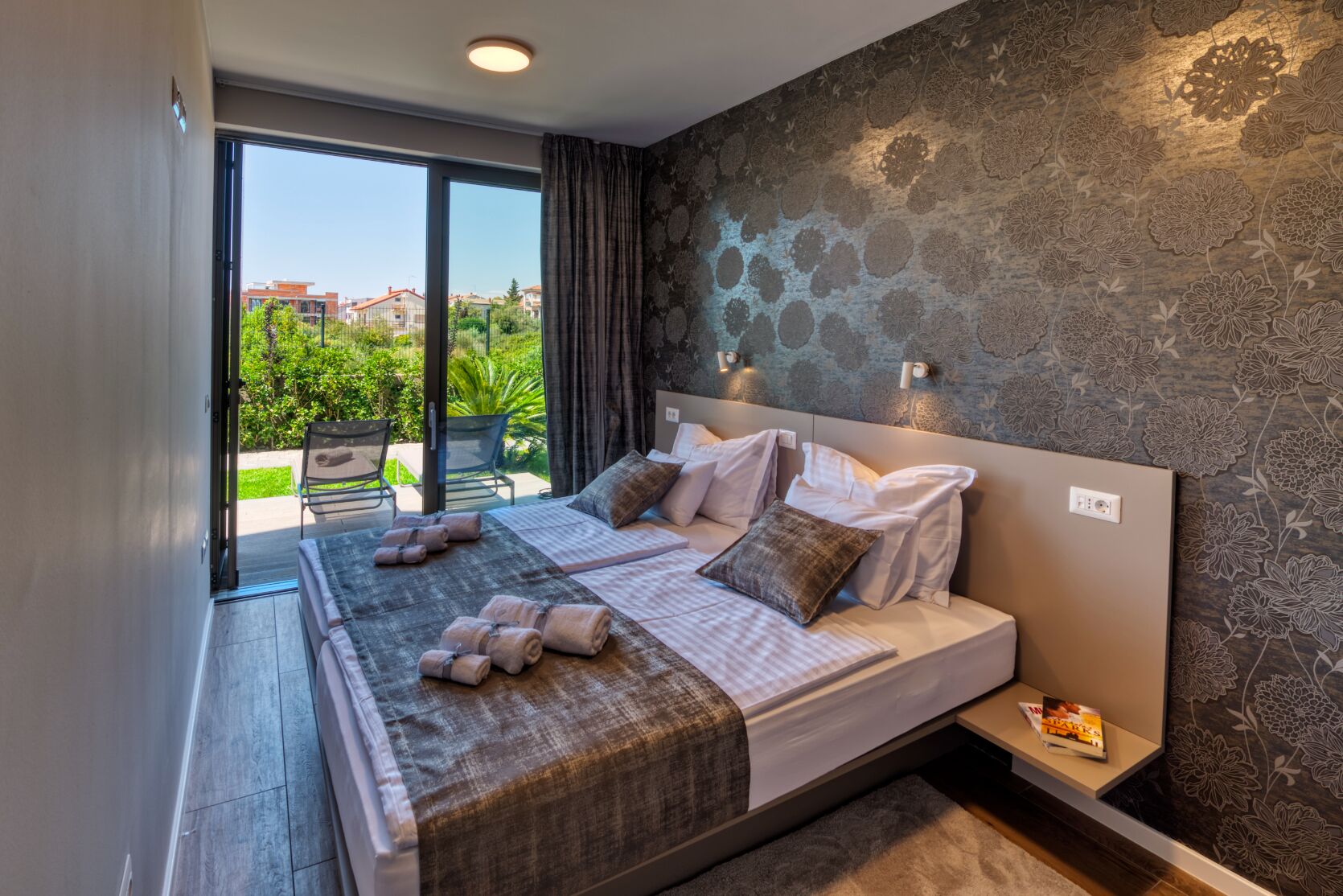 A double bed with a headboard, two bedside tables, and a view of the outdoors through a glass door.
