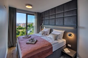 Una habitación de hotel moderna con una cama grande, vistas de la ciudad y un cabecero oscuro.