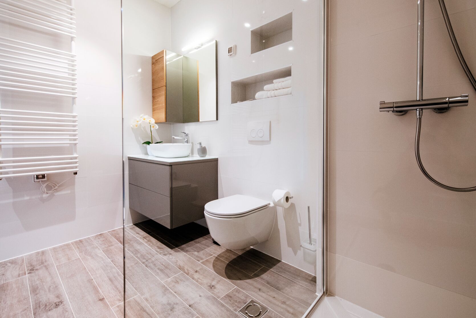 Et moderne badeværelse med en glasbrusekabine, et hvidt toilet, et vaskeskab med spejl og en håndklædestang.