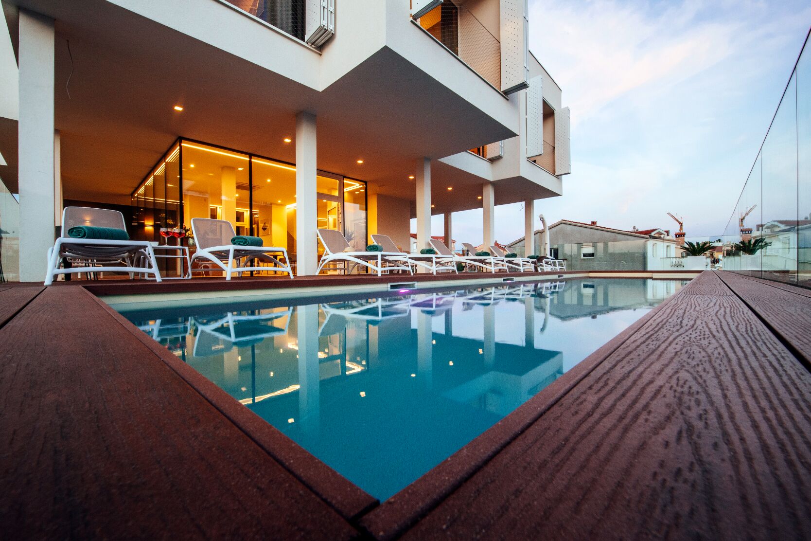 A swimming pool with lounge chairs, a building with large windows, and a clear sky.