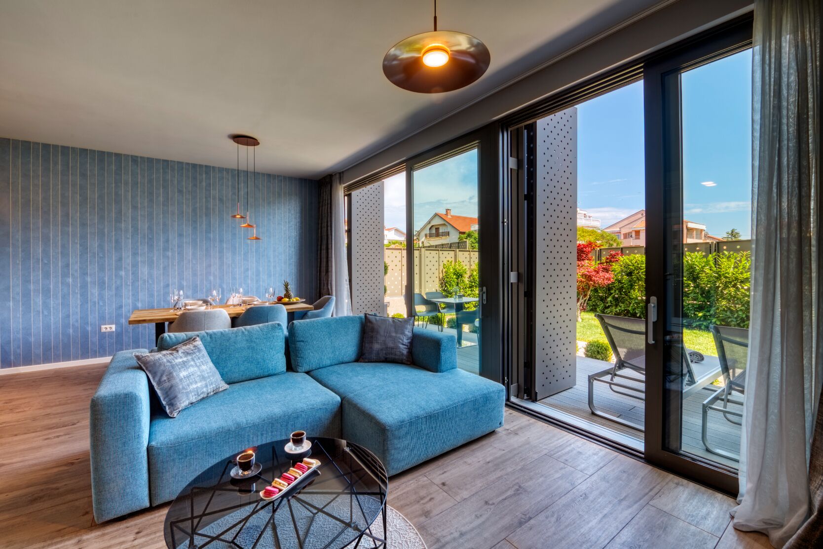 A modern living room with a blue sectional sofa, a glass coffee table, and a dining area with a wooden table and chairs.