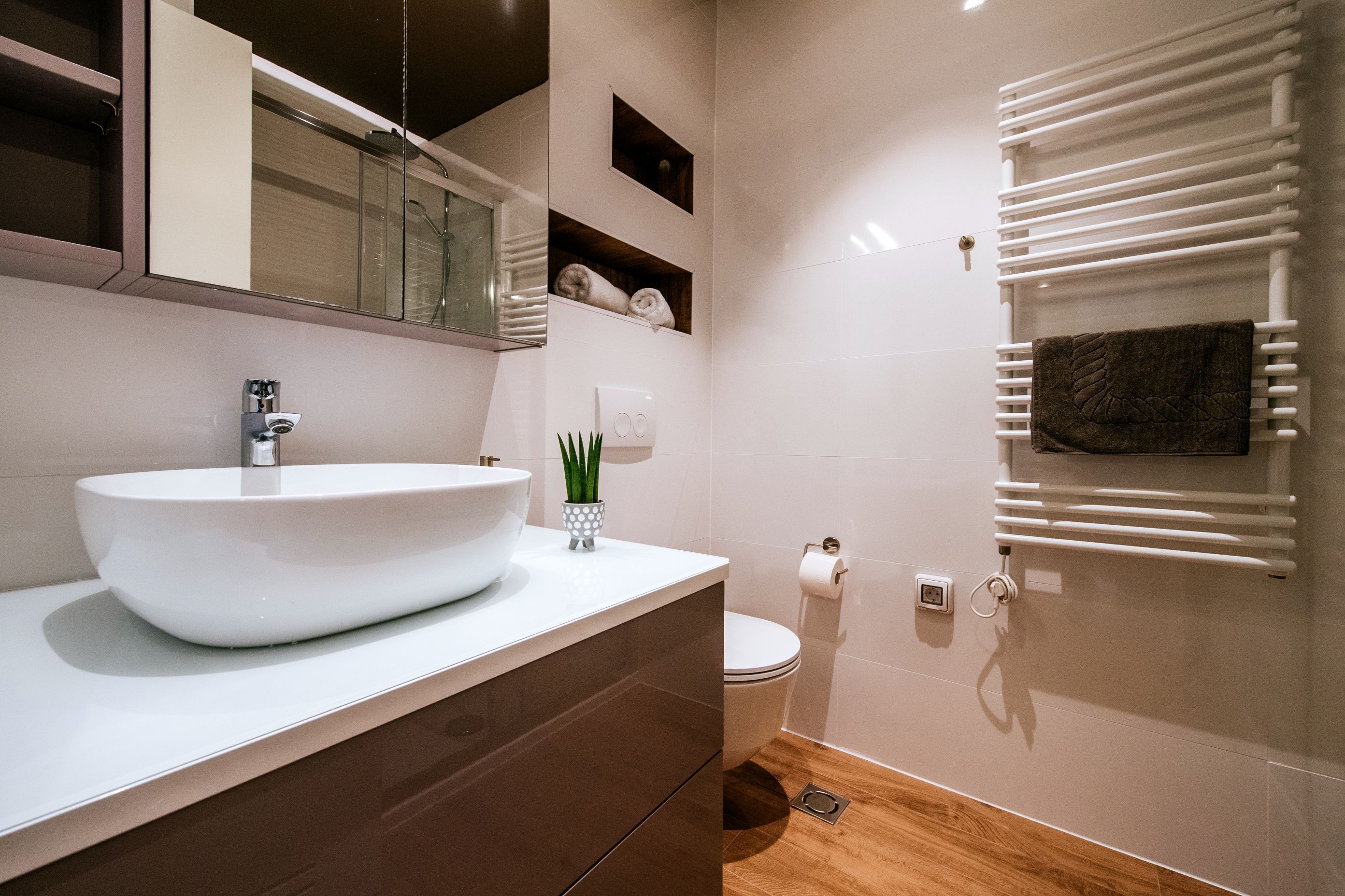 A modern bathroom with a large white sink, a mirror, a towel rack, and a toilet.